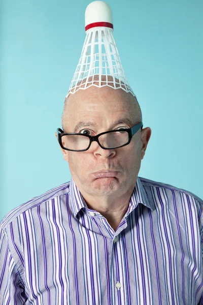 Retrato de homem sênior fazendo rosto com shuttlecock na cabeça — Fotografia de Stock