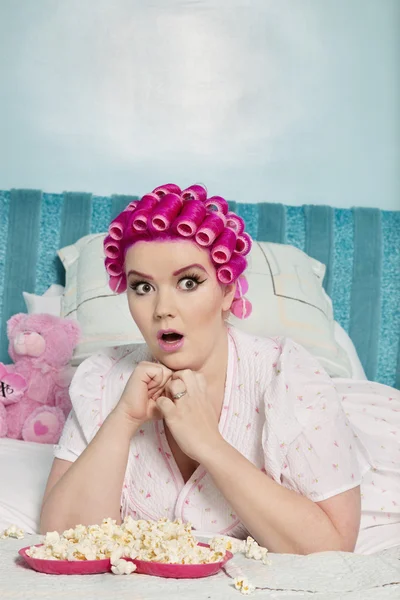 Shocked young woman with popcorn lying on bed while looking away — Stock Photo, Image