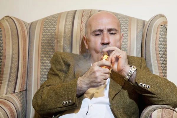 Зрілий чоловік запалює сигару, сидячи на кріслі — стокове фото