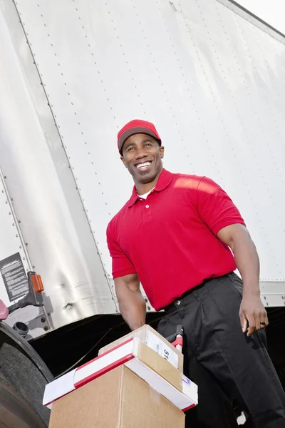 Vrolijke jonge bezorger duwen handtruck — Stockfoto