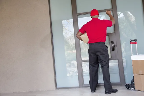 Vista trasera de un repartidor con paquetes llamando a la puerta — Foto de Stock