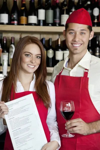 Portrait of young wait staff with wine glass and menu card in bar — Stock Photo, Image