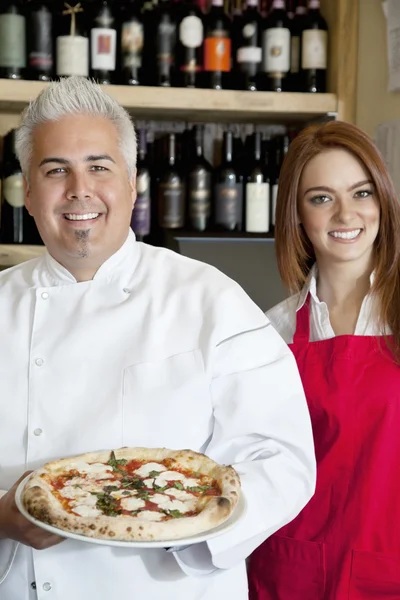 Retrato de um chef feliz segurando pizza com bela garçonete — Fotografia de Stock