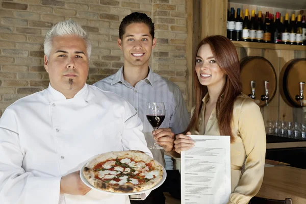 Portrait de jeune couple heureux avec chef tenant une pizza — Photo