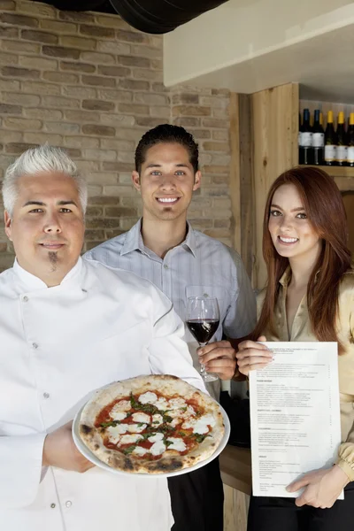 Portrait de chef heureux tenant pizza avec jeune couple — Photo