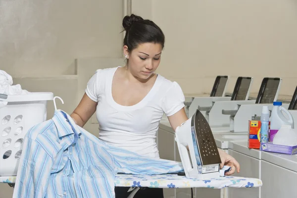 Joven empleada planchando ropa en lavandería —  Fotos de Stock