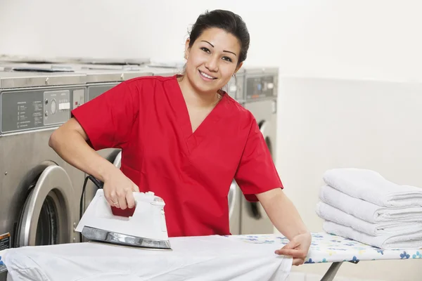 Retrato de una empleada feliz en uniforme rojo planchando ropa en lavandería —  Fotos de Stock