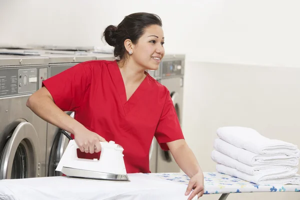 Glückliche junge Mitarbeiterin bügelt, während sie im Waschsalon wegschaut — Stockfoto