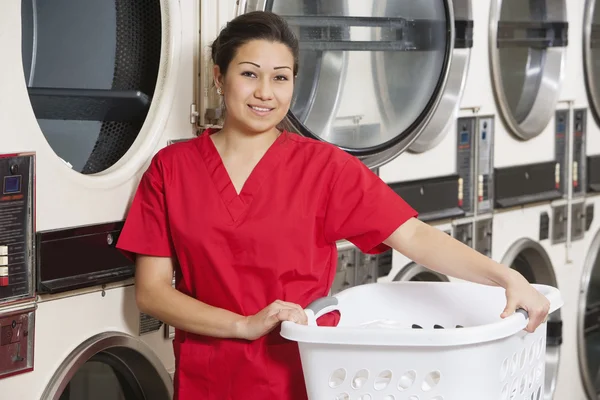 Retrato de una mujer feliz llevando una cesta de lavandería con lavadora en el fondo — Foto de Stock