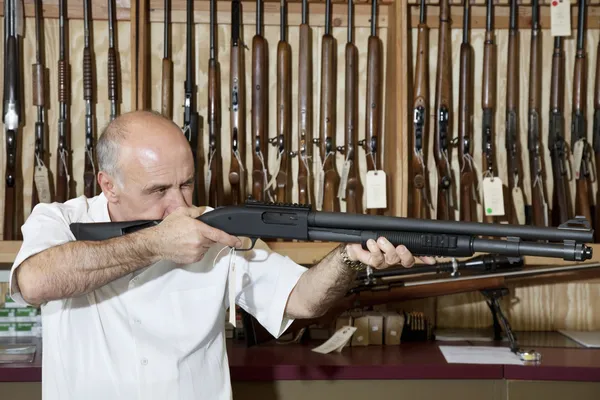 Mature gun shop merchant with rifle aiming — Stock Photo, Image