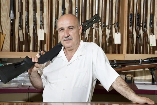 Portrait of a mature man with rifle on shoulder in gun store — Stock Photo, Image