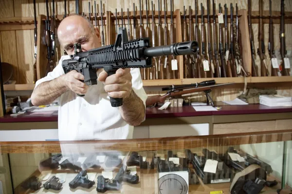 Comerciante maduro visando com rifle na loja de armas — Fotografia de Stock