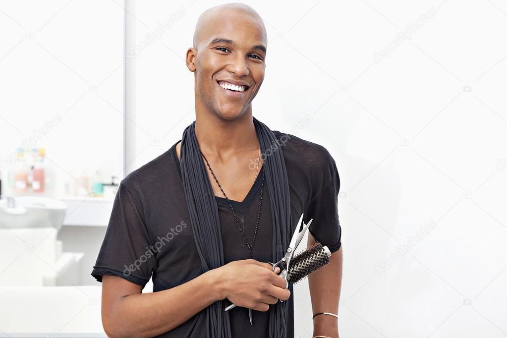 Portrait of happy male stylist holding hairbrush and scissors