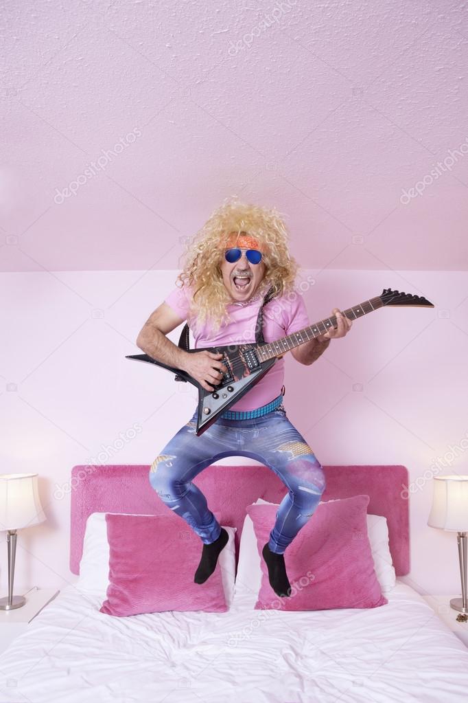 Hippie man jumping on bed while playing guitar