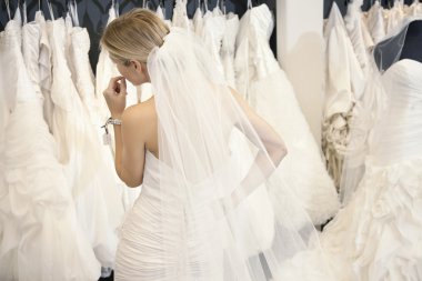 Gelinlik giymiş genç bir kadının butikte sergilenen gelinliklere bakışı.