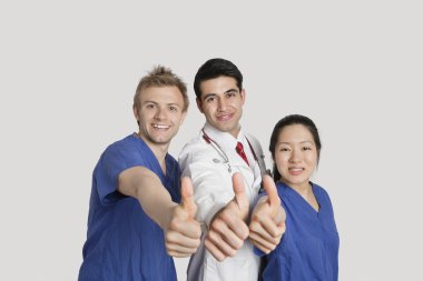 Portrait of a happy medical team gesturing thumbs up over gray background clipart