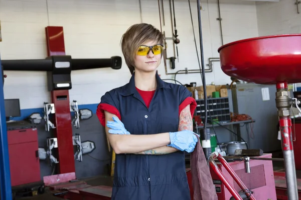 Ritratto di una giovane meccanico con indosso un equipaggiamento protettivo a braccia incrociate in officina — Foto Stock