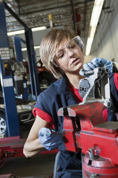 Young female mechanic in protective workwear working on machinery part in automobile repair shop — Stock Photo, Image