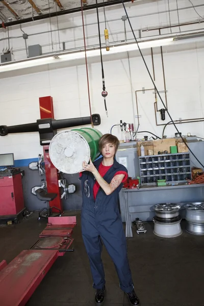 Retrato de uma jovem mecânica carregando tambor de óleo no ombro na garagem de reparação de automóveis — Fotografia de Stock