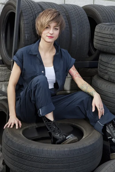 Portrait of a young mechanic sitting on tires in car workshop — Stock Photo, Image