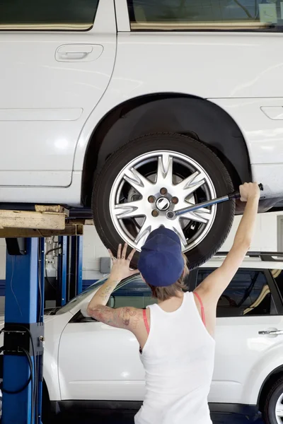 Back view of young female working on car tire in workshop — Stock Photo, Image