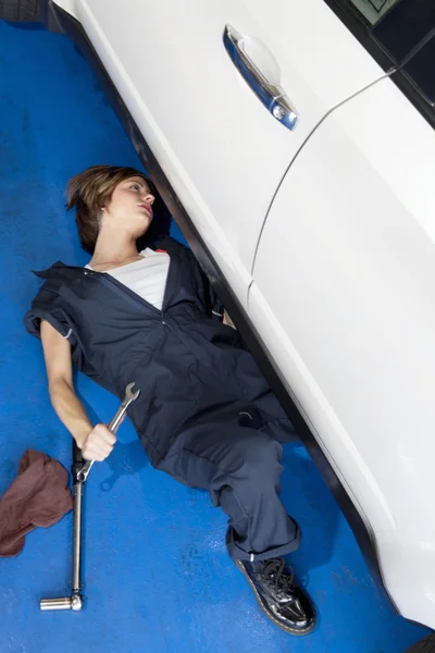 Woman lying down on floor working on car in automobile garage — Stock Photo, Image