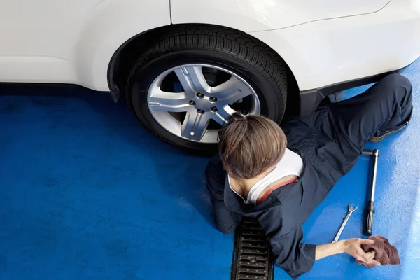 Hoge hoekmening van vrouw liggend op vloer werken op auto in werkplaats — Stockfoto