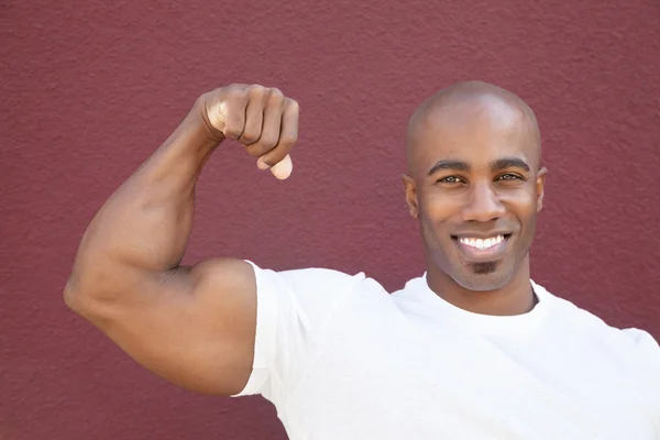 Portrait of a young African American man flexing muscles over colored background — Stock Photo, Image