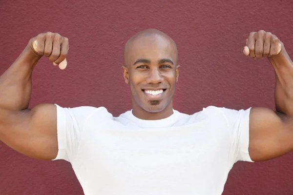 Retrato de un hombre afroamericano feliz flexionando los músculos sobre un fondo de color — Foto de Stock