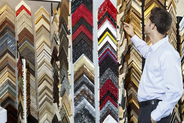 Hombre joven mirando marcos multicolores en la tienda — Foto de Stock