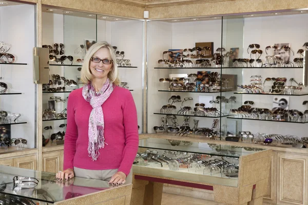 Portret van een gelukkig senior vrouwelijke opticien permanent in winkel — Stockfoto