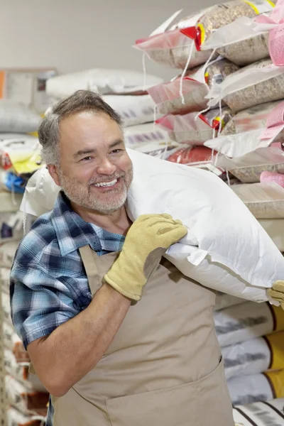 Feliz vendedor maduro llevando saco en la tienda de piensos —  Fotos de Stock
