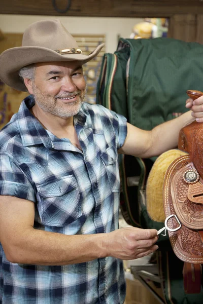 Portret van een gelukkig cowboy met paardrijden tack in diervoeders winkel — Stockfoto