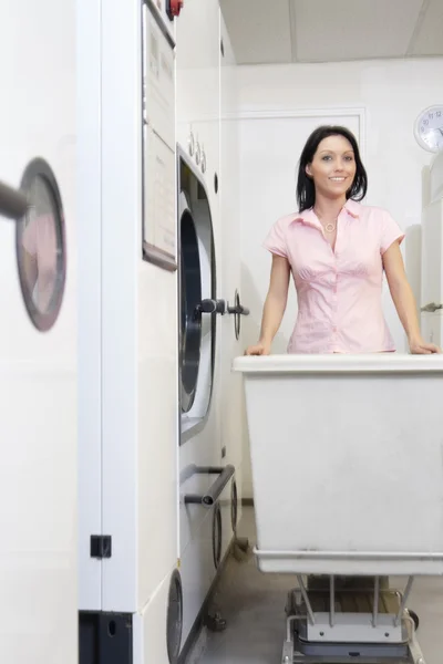 Retrato de uma mulher adulta média feliz empurrando carrinho na lavanderia — Fotografia de Stock