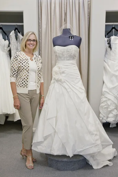 Retrato de una mujer feliz de pie junto a un elegante vestido de novia en boutique — Foto de Stock