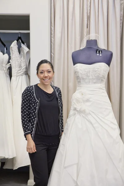 Porträt einer reifen Angestellten, die neben einem eleganten Hochzeitskleid im Brautladen steht — Stockfoto