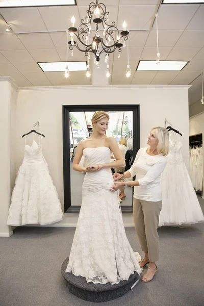 Hermosa mujer vestida como novia con empleado senior ayudando en la tienda nupcial — Foto de Stock