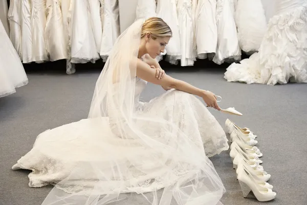 Vista laterale della giovane donna in abito da sposa confuso durante la selezione di calzature — Foto Stock