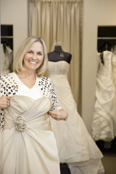 Retrato de una mujer mayor feliz sosteniendo vestido de novia en la tienda nupcial — Foto de Stock