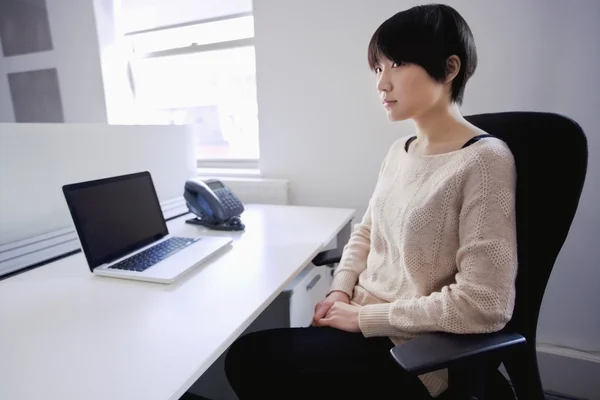 Mulher asiática sentada na mesa com laptop enquanto olha para longe — Fotografia de Stock