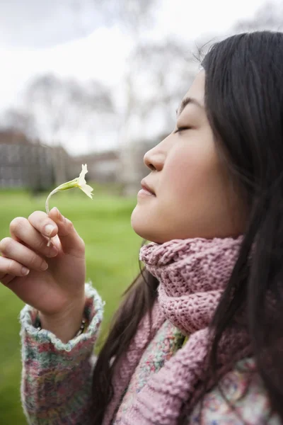 Vista lateral de uma jovem mulher asiática cheirando flor no parque — Fotografia de Stock