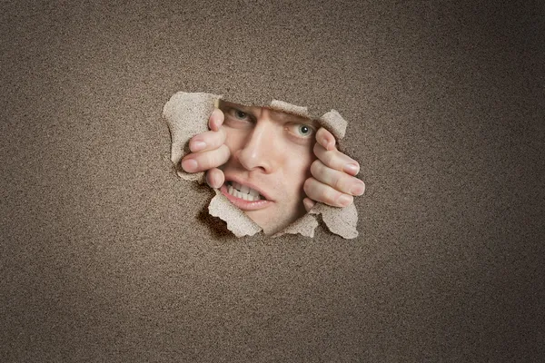 Retrato de um homem adulto médio agressivo espreitando do buraco rasgado do papel branco — Fotografia de Stock