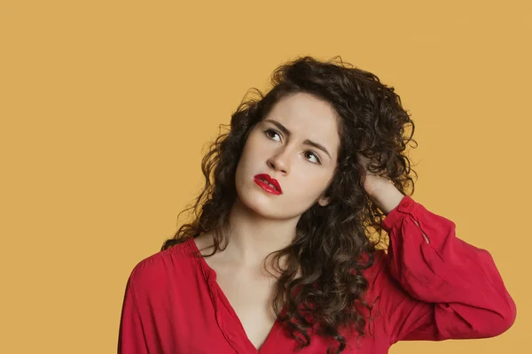 Thoughtful young woman with hand in hair over colored background — Stock Photo, Image