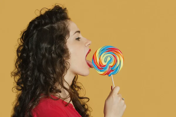 Genç kadın yalama lolipop renkli arka plan üzerinde yan görünüm — Stok fotoğraf
