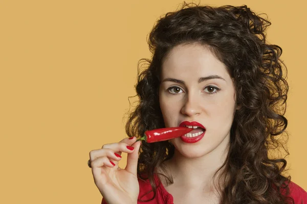 Retrato de uma jovem mulher mordendo pimenta vermelha sobre fundo colorido — Fotografia de Stock