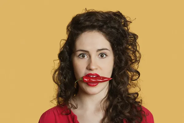 Portret van een jonge vrouw met rode chili peper in mond over gekleurde achtergrond — Stockfoto