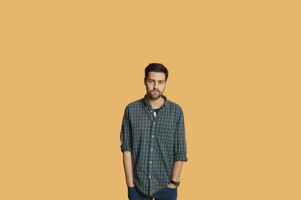 Porträtt av en ung man som står med händerna i fickorna på färgad bakgrund — Stockfoto