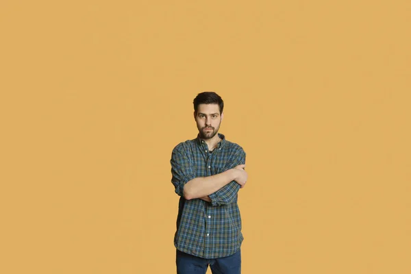 Portrait of a confident young man standing with arms crossed over colored background — Stock Photo, Image