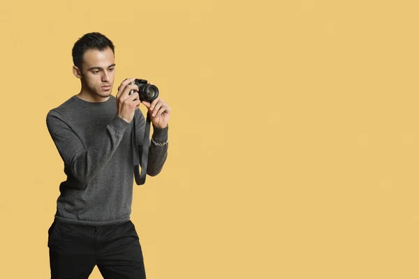 Zelfverzekerde jonge man met digitale camera over gekleurde achtergrond — Stockfoto