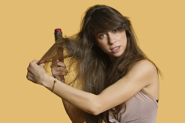 Portrait of a young woman brushing hair over colored background — Stock Photo, Image